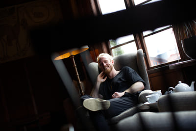 Fredrik Brännlund leaning back in an armchair with his legs drawn up, a teapot in the foreground