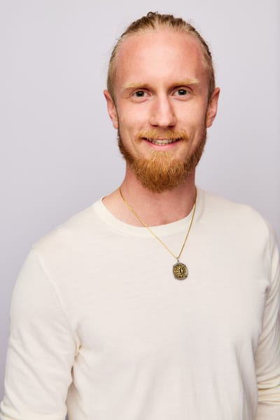 Fredrik Brännlund smiling at the camera in a light knitted sweater against a pale lilac backdrop