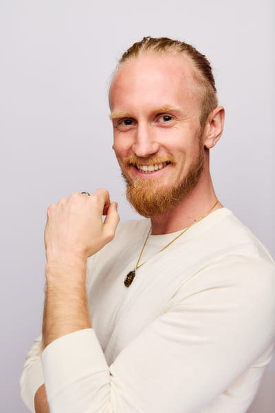 Fredrik Brännlund laughing with a closed fist at his chin, in a light knitted sweater